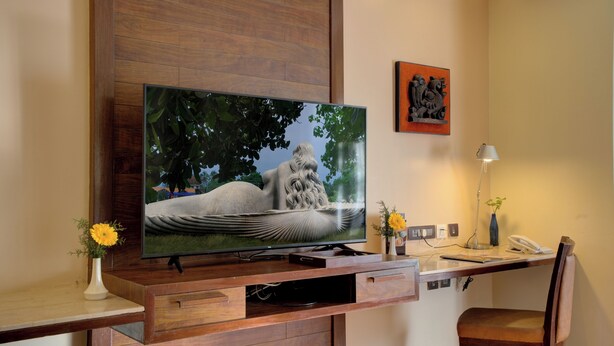 A flat-screen TV mounted on a wooden TV stand with a desk and chair below. - Hotel Tamilnadu Pandiyan Madurai (Madurai)