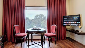 A room with a TV displaying a streaming service interface, a round table with two chairs, and a window with curtains. - Hotel Tamilnadu Pandiyan Madurai (Madurai)