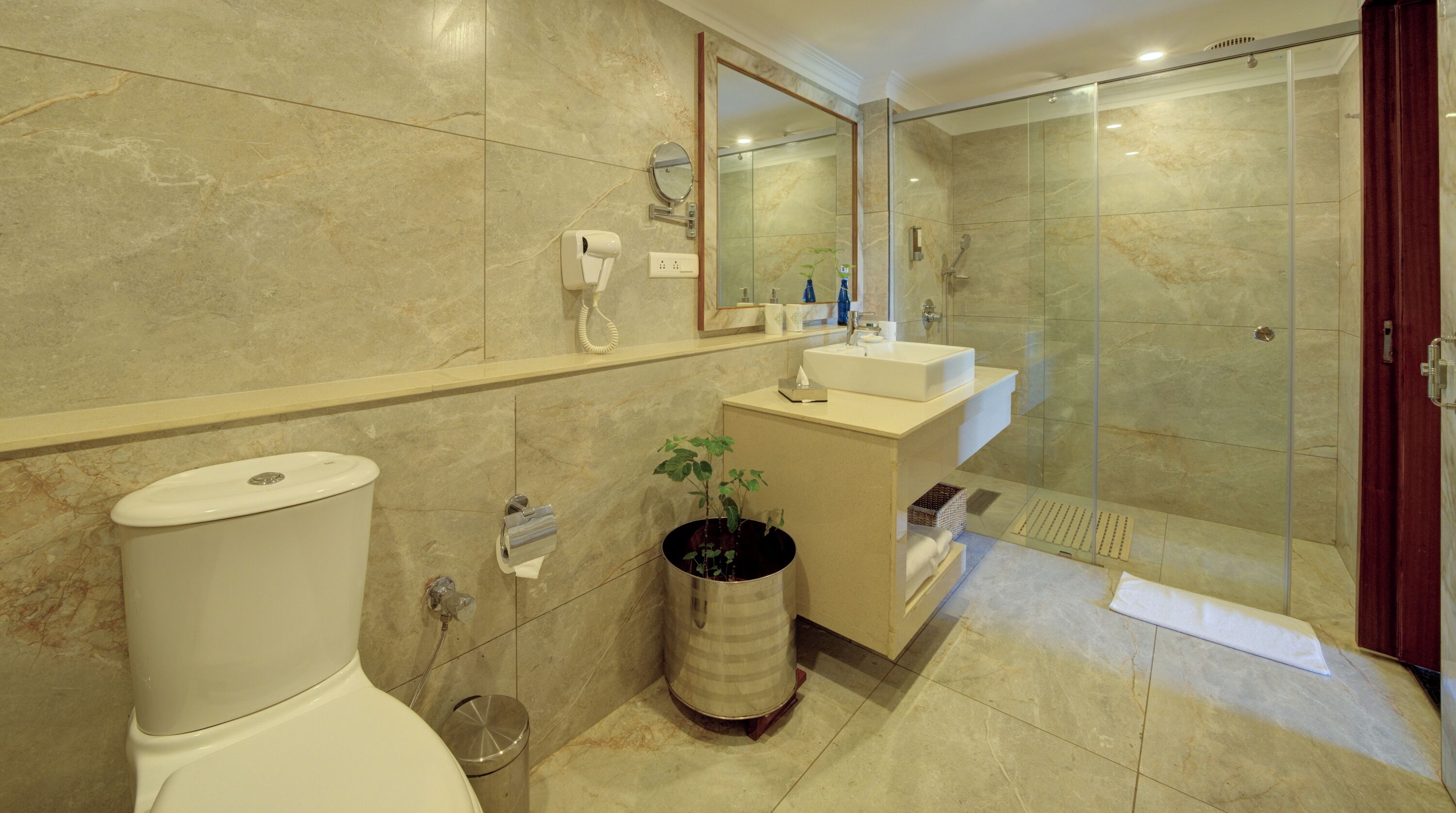 Een moderne badkamer met toilet, wastafel, douche en een kamerplant.