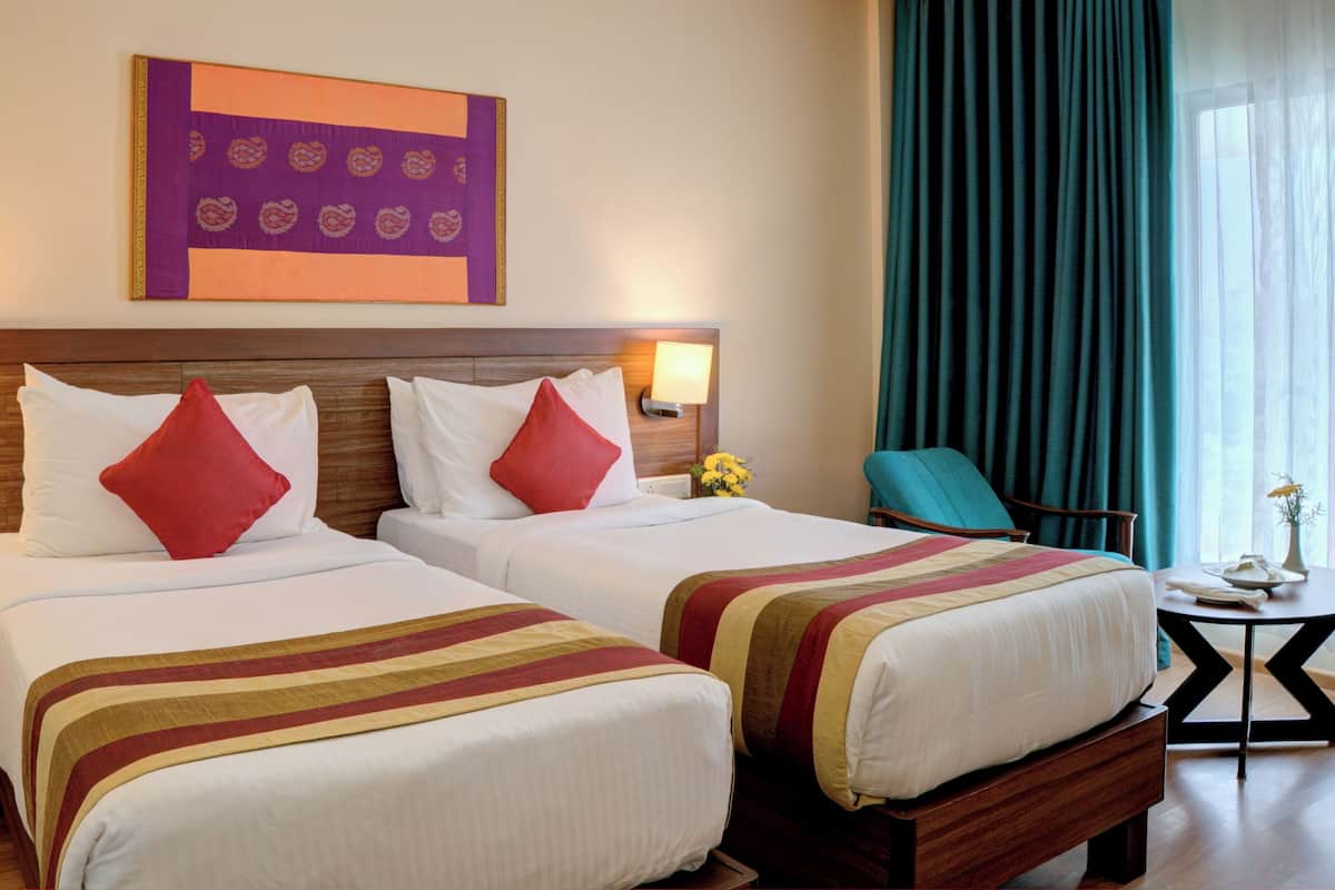 Una habitación de hotel con dos camas, una mesita de noche, una lámpara, una silla y una pequeña mesa con un florero.