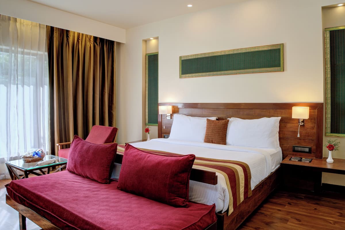 Habitación de hotel con cama, dos mesitas de noche, una silla, una mesita pequeña y una ventana con cortinas.