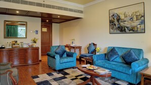 A room with two blue armchairs, a wooden coffee table, a painting on the wall, and a wooden cabinet with various items on top. - Hotel Tamilnadu Pandiyan Madurai (Madurai)