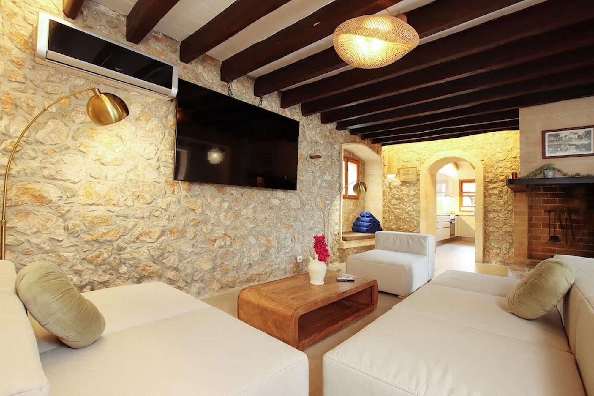 A living room with stone walls, a flat-screen TV, a wooden coffee table, and white sofas.