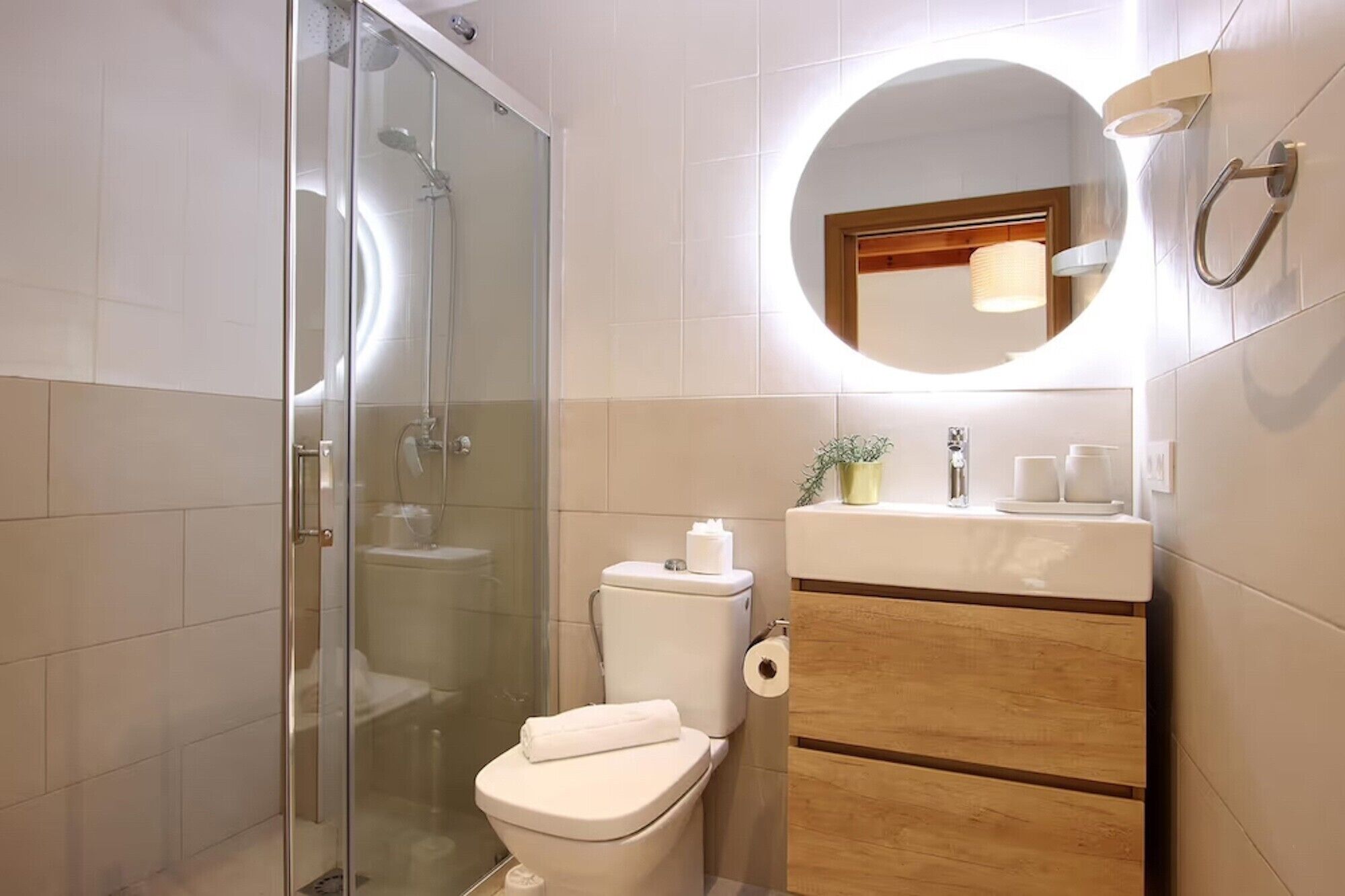 A bathroom with a glass-enclosed shower, a toilet with a towel on it, a sink with a mirror above, and a wooden cabinet below.