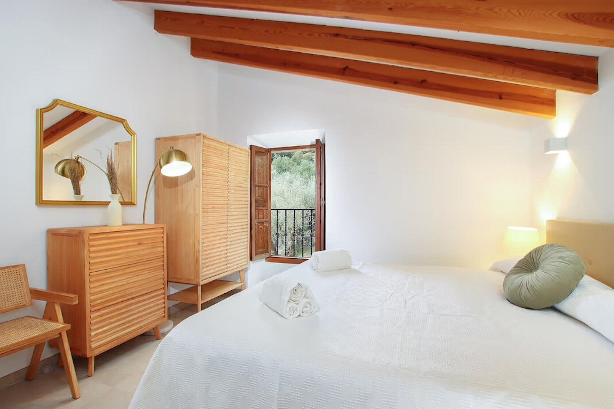 Une chambre à coucher avec un lit, une commode en bois, une chaise et un balcon avec vue.