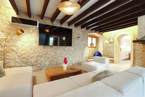 A modern living room with stone walls, a flat-screen TV, a sofa, and a wooden coffee table. - Holiday Home "Alordes" with Mountain View, Pool, Garden & Wi-Fi (Illes Balears)