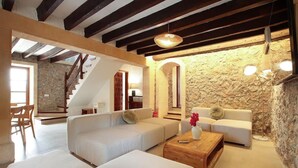 A spacious living area with a stone wall, a wooden staircase, and a modern sofa set. - Holiday Home "Alordes" with Mountain View, Pool, Garden & Wi-Fi (Illes Balears)