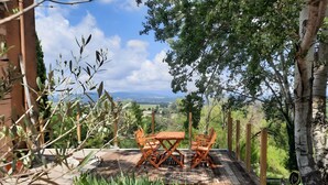 A wooden deck with a table and chairs, surrounded by greenery and overlooking a landscape.