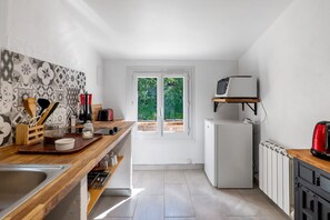 Une cuisine de taille réduite, dotée d’un plan de travail en bois, d’un réfrigérateur blanc et d’une fenêtre donnant sur un paysage verdoyant.