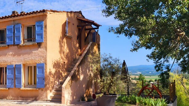 A rustic building with a stone staircase, a large potted plant, and a view of the countryside.