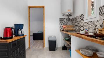 Une petite cuisine équipée d’une machine à café, d’une bouilloire et d’une poubelle. La pièce adjacente contient un lit et un radiateur est fixé au mur.