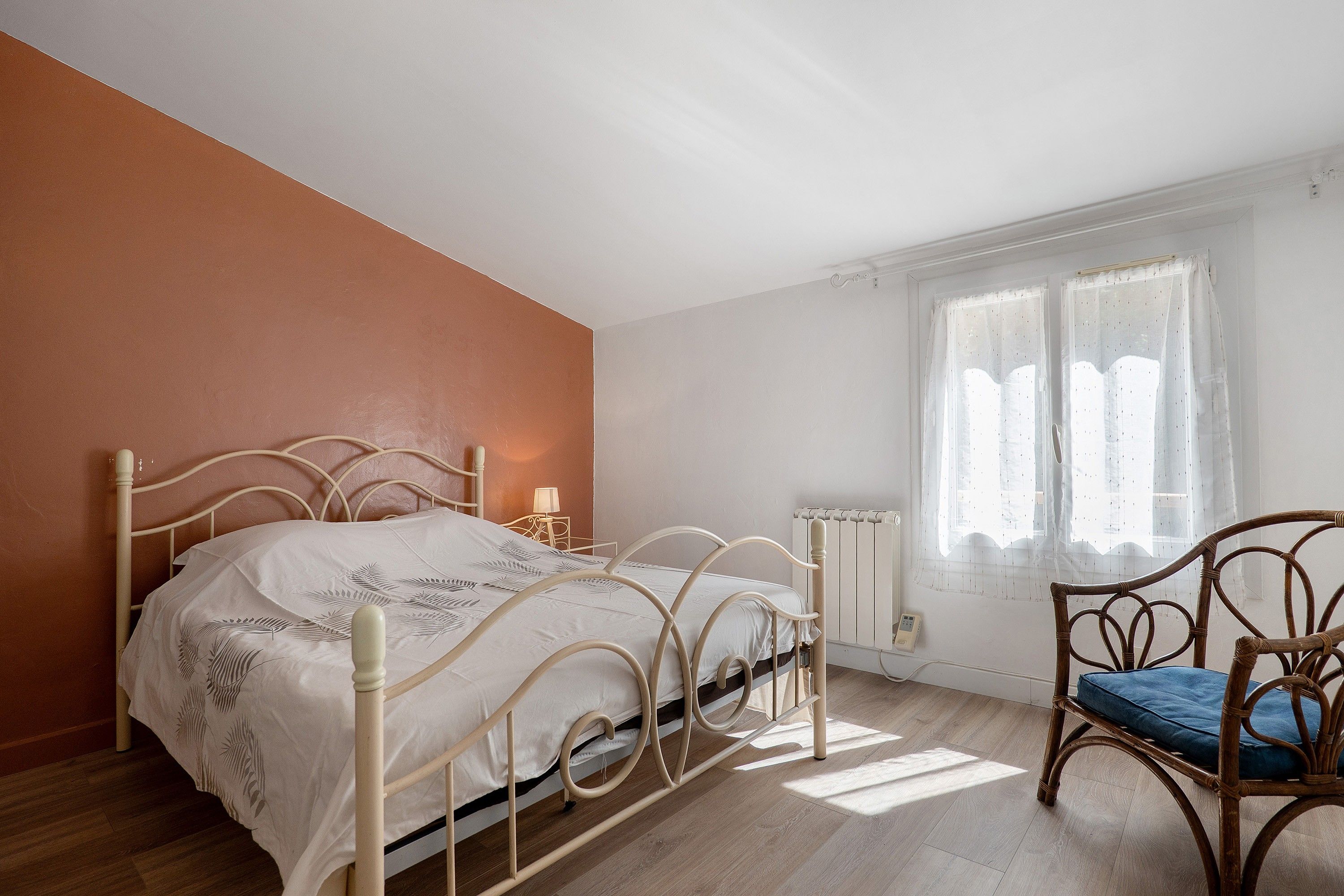 Une chambre à coucher avec un lit, une chaise, une fenêtre avec des rideaux et un radiateur.
