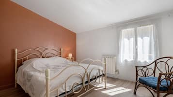 Une chambre à coucher avec un lit, une chaise, une fenêtre avec des rideaux et un radiateur.