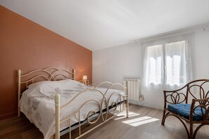 Un dormitorio con cama, una silla, un ventanal con cortinas y un radiador.