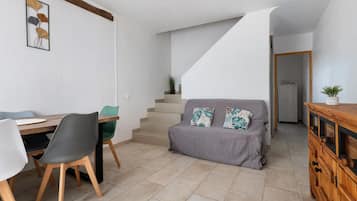 A dining area with a wooden table and chairs, a staircase leading to an upper level, and a grey sofa with patterned cushions.
