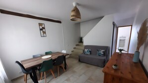 Un coin repas avec une table et des chaises en bois, un canapé gris agrémenté de coussins décoratifs, un escalier et un meuble en bois surmonté d’un vase.
