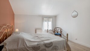 Ein Schlafzimmer mit einem Bett, einem Sessel, einem Fenster, einer Heizung und einem Spiegel an der Wand.