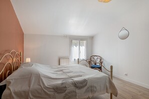 Ein Schlafzimmer mit einem Bett, einem Sessel, einem Fenster, einer Heizung und einem Spiegel an der Wand.