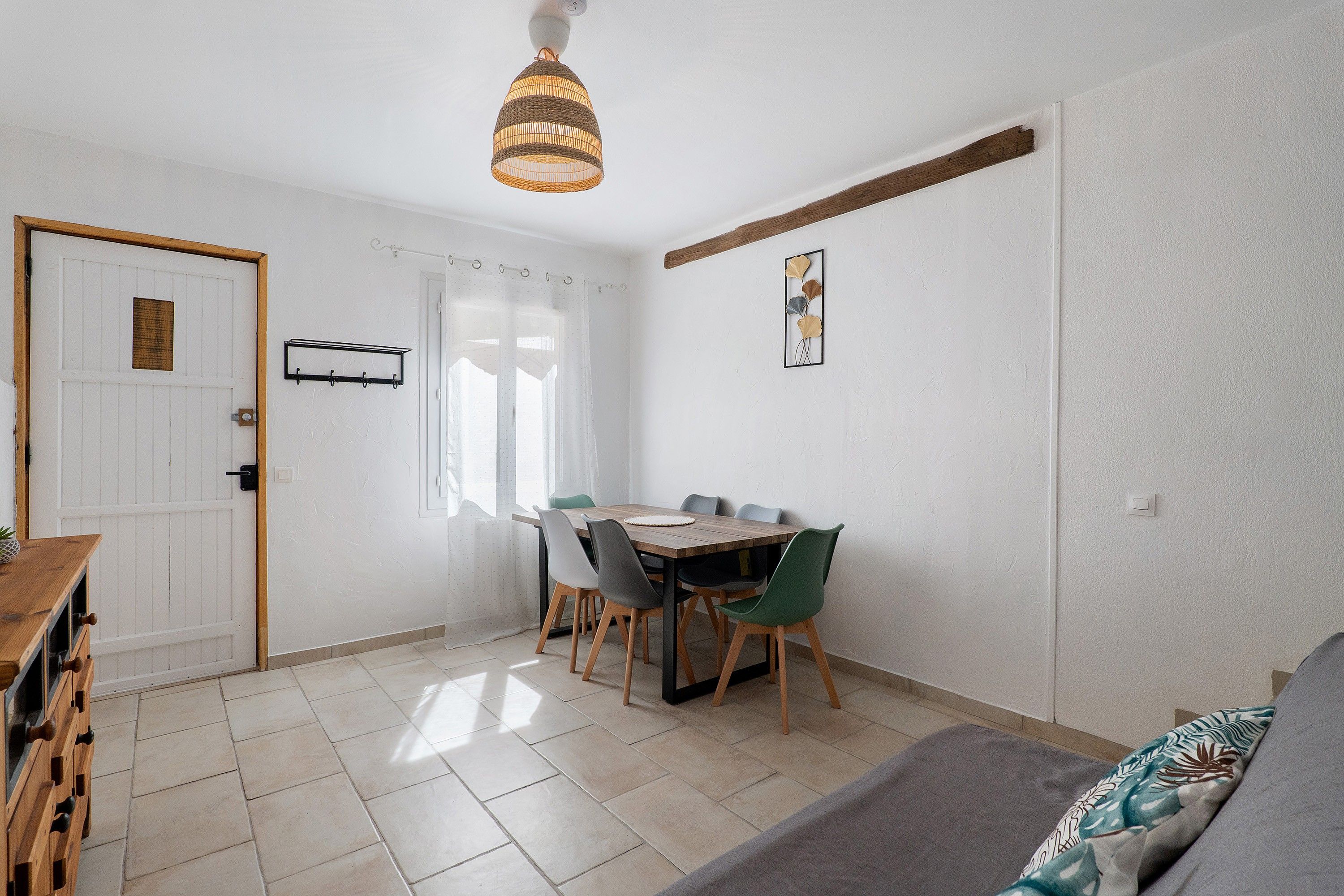 A room with a dining table, chairs, a sofa, a hanging light fixture, and a door.