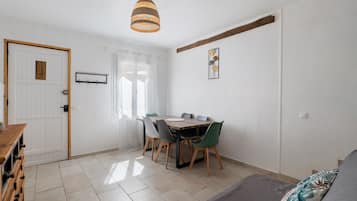 A room with a dining table, chairs, a sofa, a hanging light fixture, and a door.