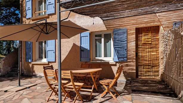 Eine Terrasse mit Tisch und Stühlen, ein Holzzaun und ein Gebäude mit blauen Fensterläden.