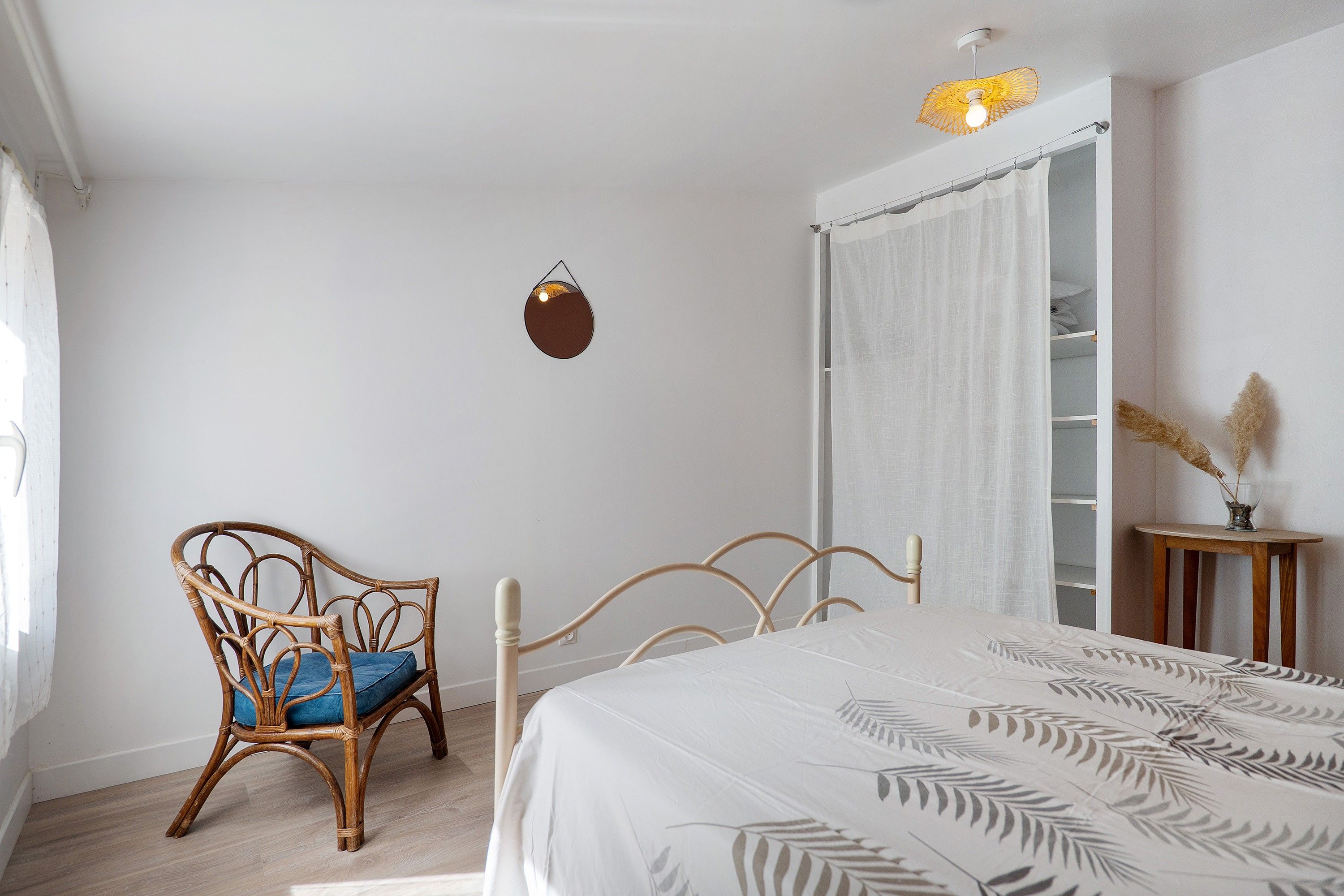 A bedroom with a bed, a chair, a bedside table, a wardrobe, and a hanging light fixture.