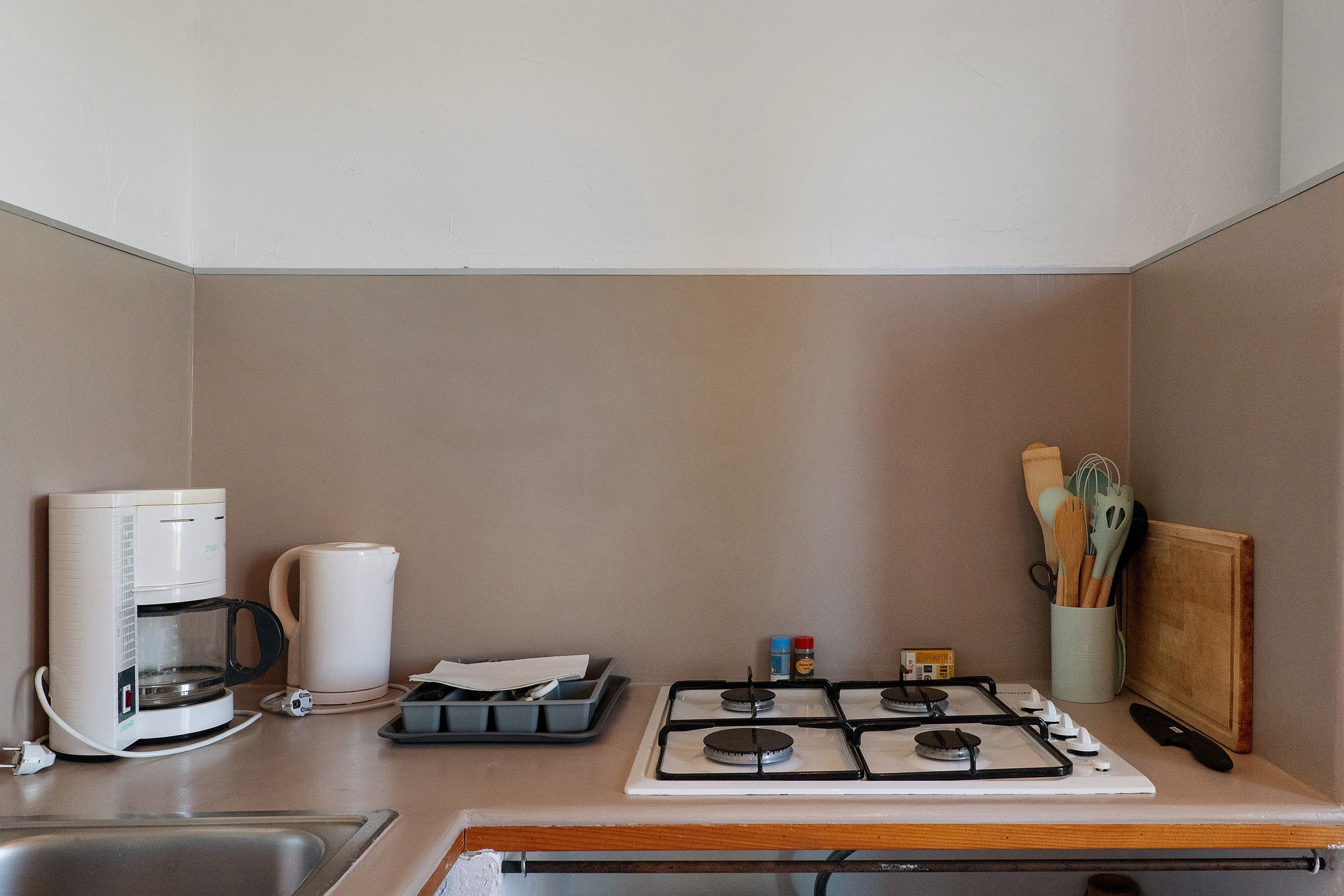 Una cucina compatta con macchina da caffè, bollitore, fornello a gas e spezieria.