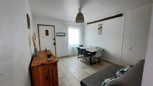 Une pièce comprenant un bureau en bois, une table à manger avec des chaises, un canapé et un luminaire suspendu.