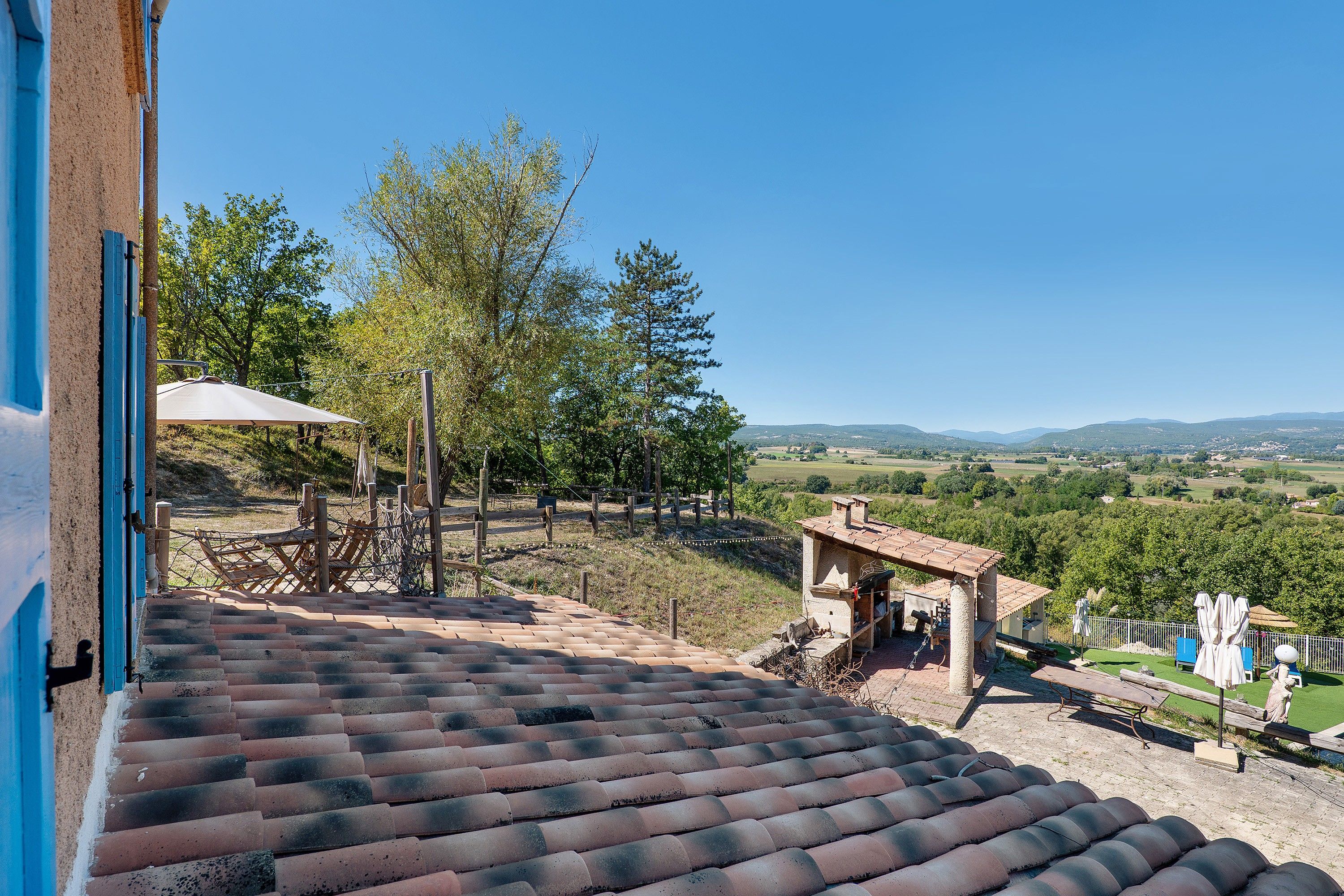 A terrace with a view of a rural landscape, a wooden structure, and a white umbrella.