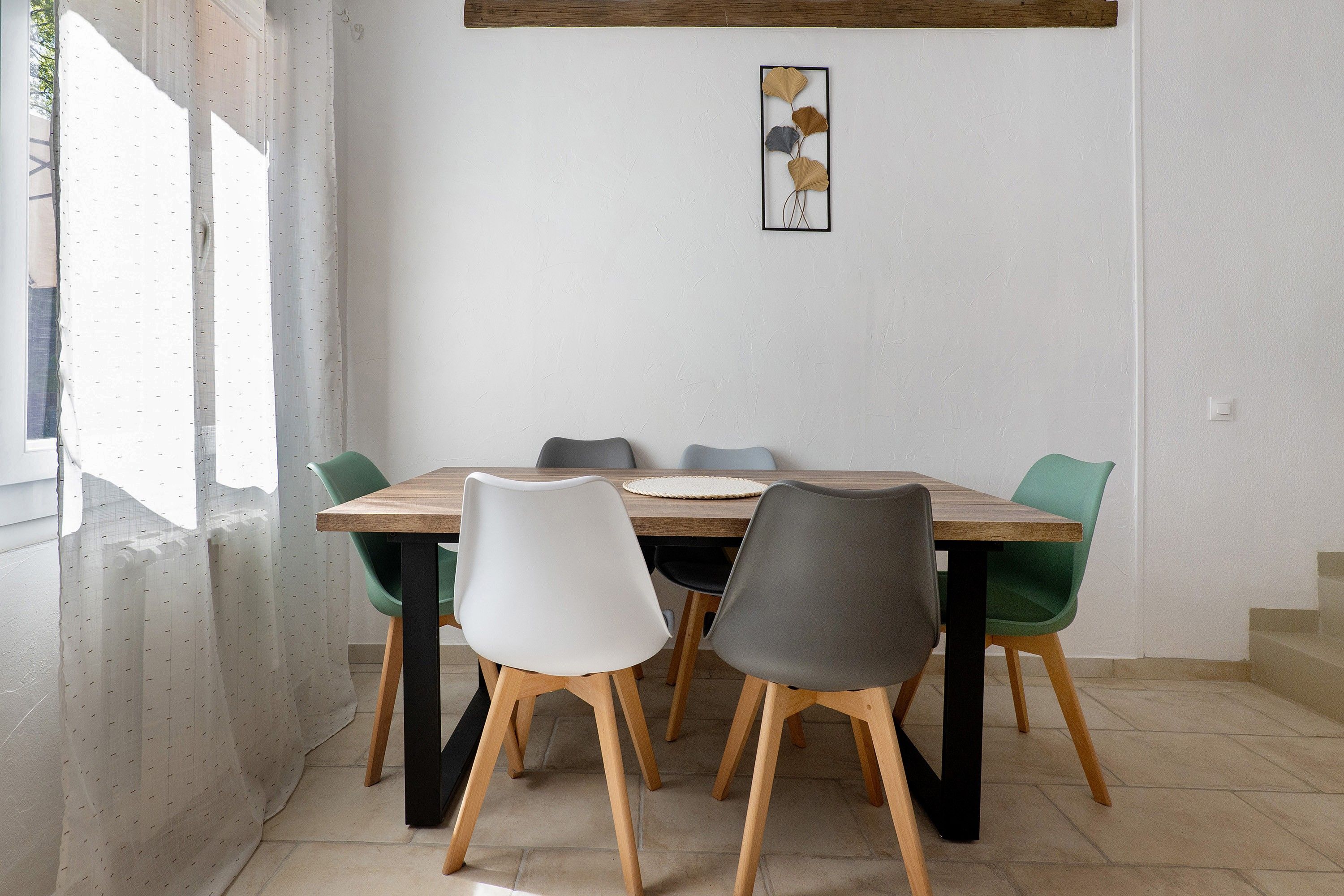 Un coin repas avec une table et des chaises en bois, une œuvre d’art accrochée au mur et une fenêtre avec des rideaux.