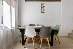 Un comedor con una mesa y sillas de madera, una obra de arte en la pared y un ventanal con cortinas.
