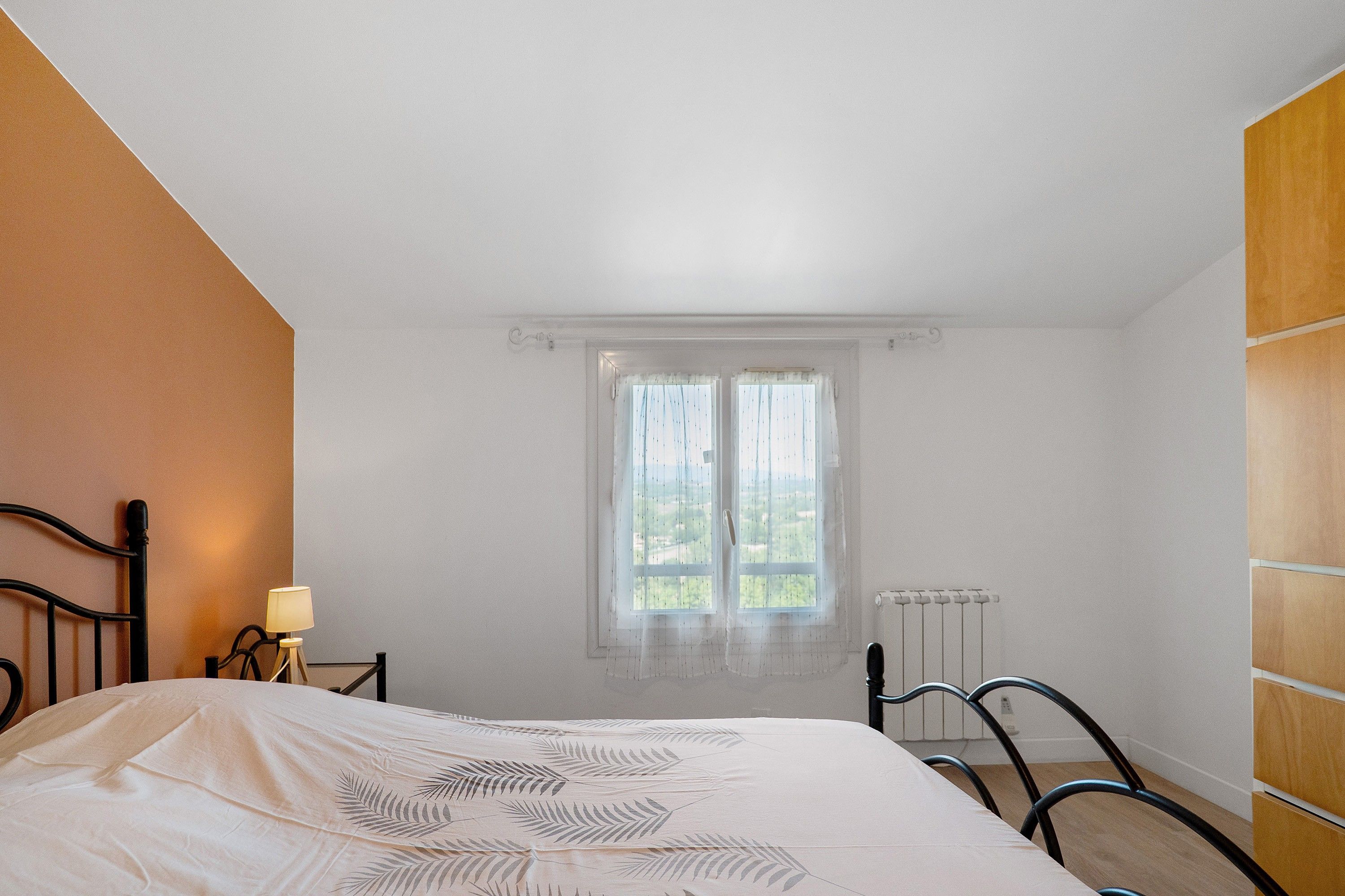 Un dormitorio con cama, mesita de noche, lámpara, ventana con cortinas y radiador.