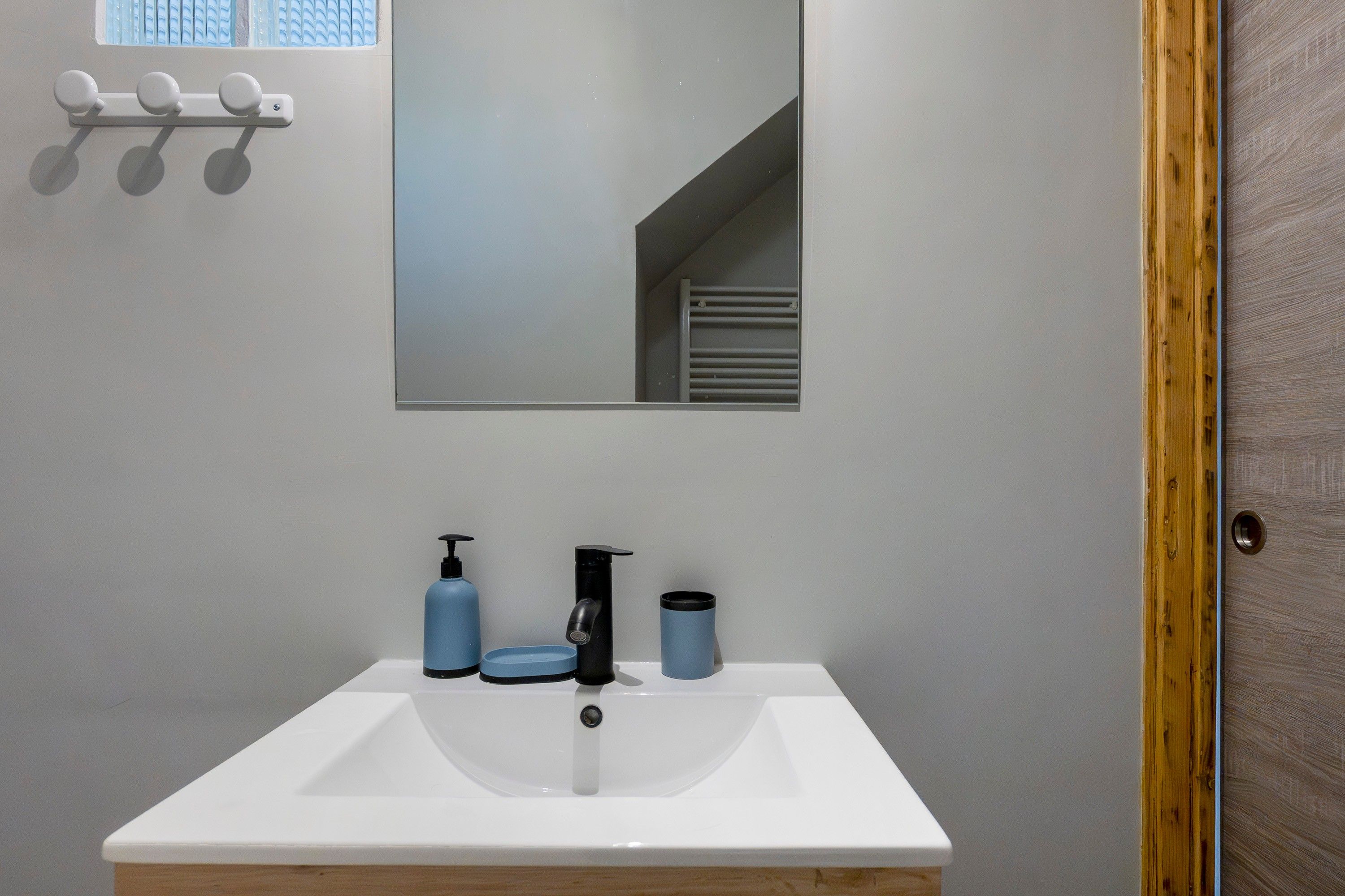Une salle de bain avec un lavabo blanc, un miroir et une fenêtre avec des stores.