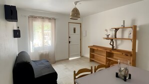 Ein Zimmer mit Bett, Tisch mit Stühlen, einem an der Wand befestigten Fernseher und einer Tür zu einem anderen Raum.