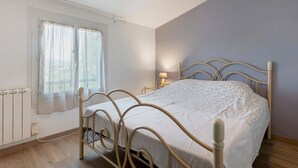 Une chambre à coucher avec un lit, une fenêtre avec des rideaux, une lampe de chevet et un radiateur.