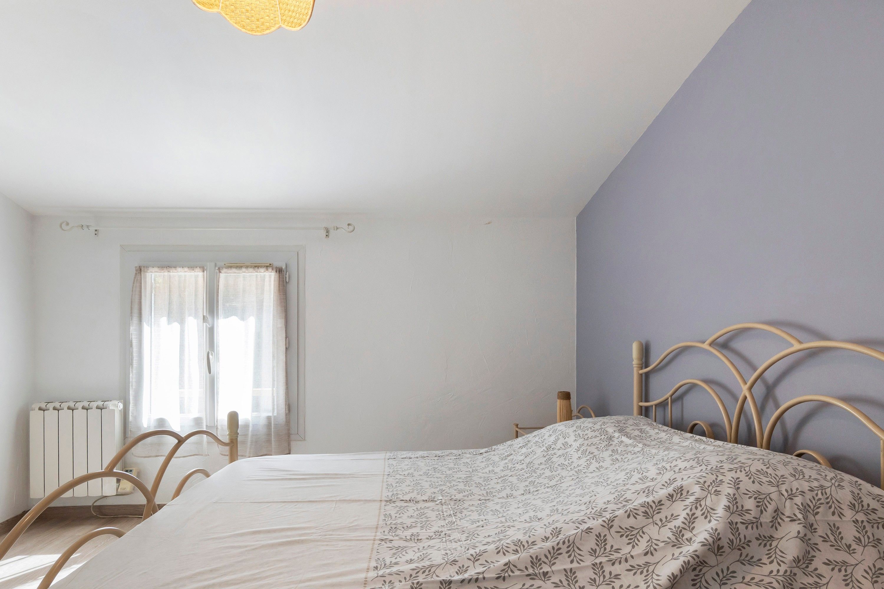 A bedroom with a bed, a radiator, a window with curtains, and a door.