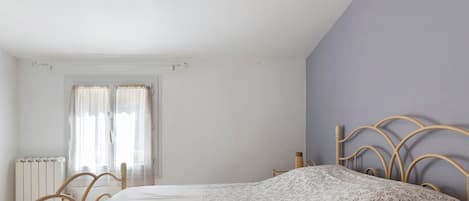 A bedroom with a bed, a radiator, a window with curtains, and a door.