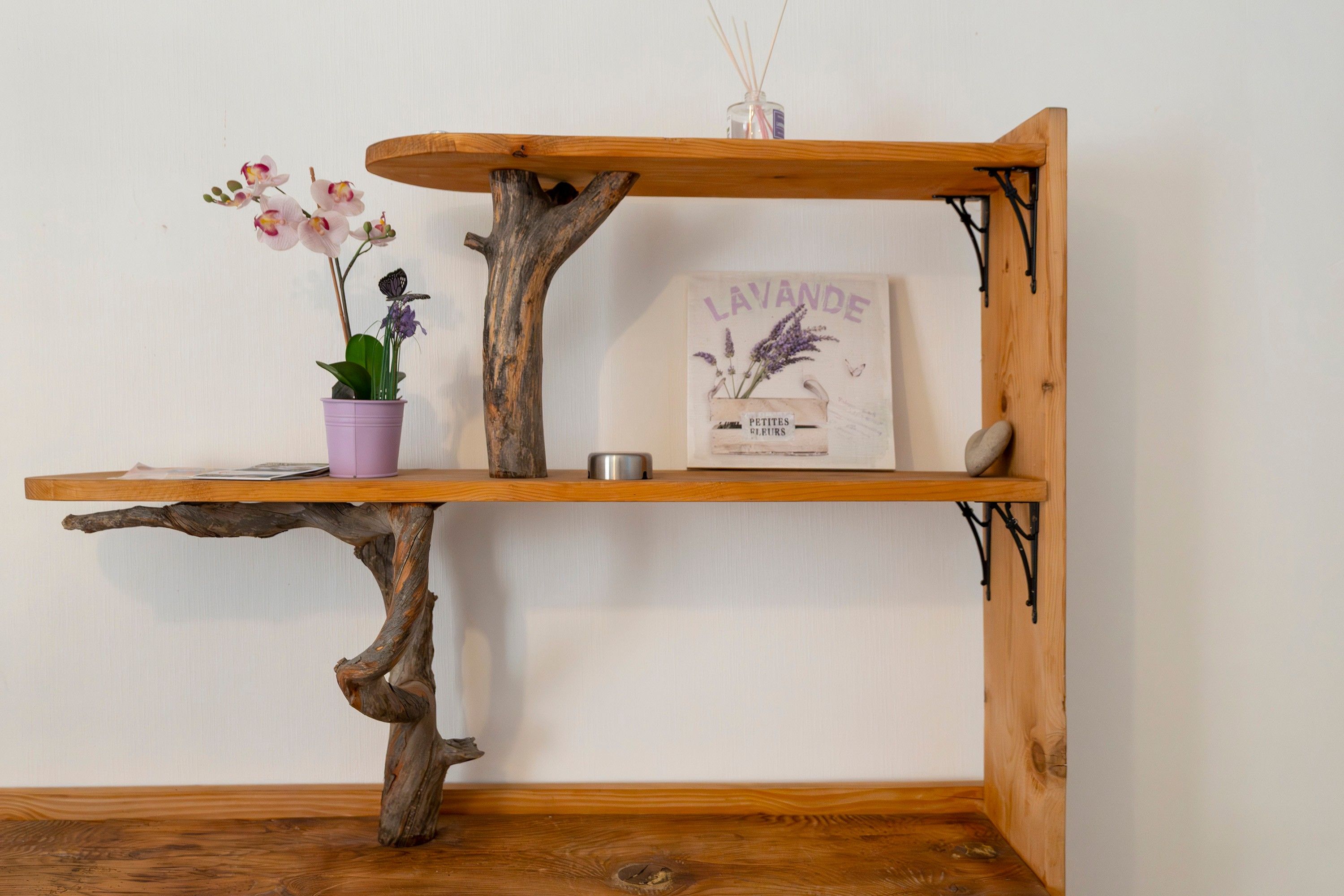 A wooden shelf with a branch base, a potted orchid, a lavender sign, and a small container.