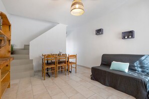 Ein Wohnzimmer mit Treppe, einem Esstisch mit Stühlen, einer Couch mit Kissen sowie zwei an Wänden befestigten Regalen mit Pflanzen.