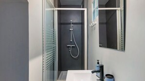 Une salle de bain moderne avec une douche à parois de verre, un lavabo blanc et un miroir.