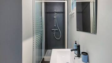 Un baño moderno con cabina de ducha de vidrio, lavabo blanco y espejo.