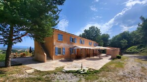 Ein zweistöckiges Gebäude mit einer Terrasse, Gartenmöbeln und Blick auf die Landschaft.
