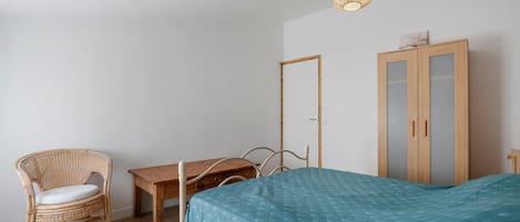 Un dormitorio con una cama, una silla, una mesita y un armario.