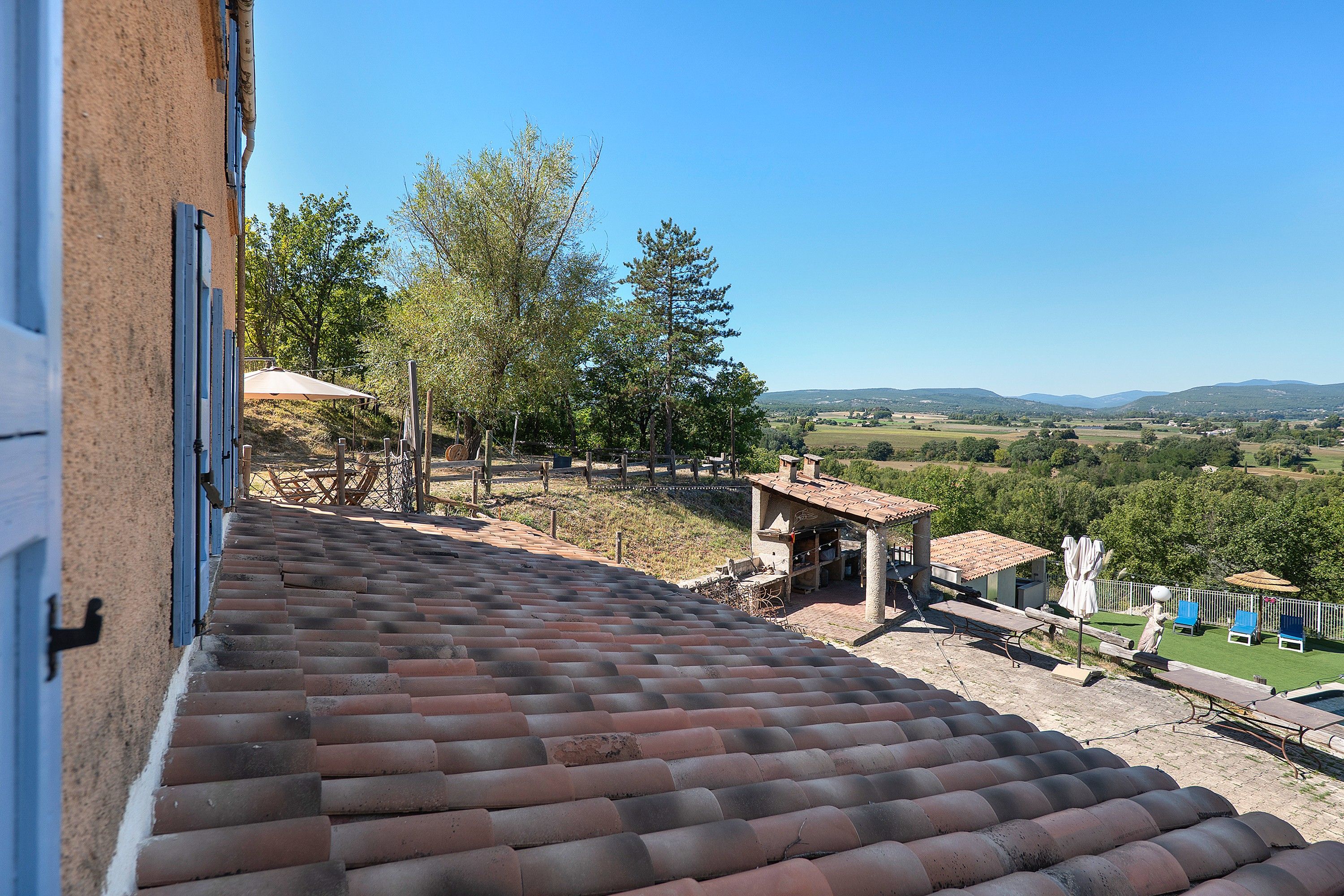 A terracotta-tiled roof, outdoor seating area with tables and chairs, and a view of a rural landscape with trees and hills.