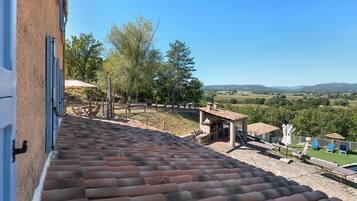A terracotta-tiled roof, outdoor seating area with tables and chairs, and a view of a rural landscape with trees and hills.