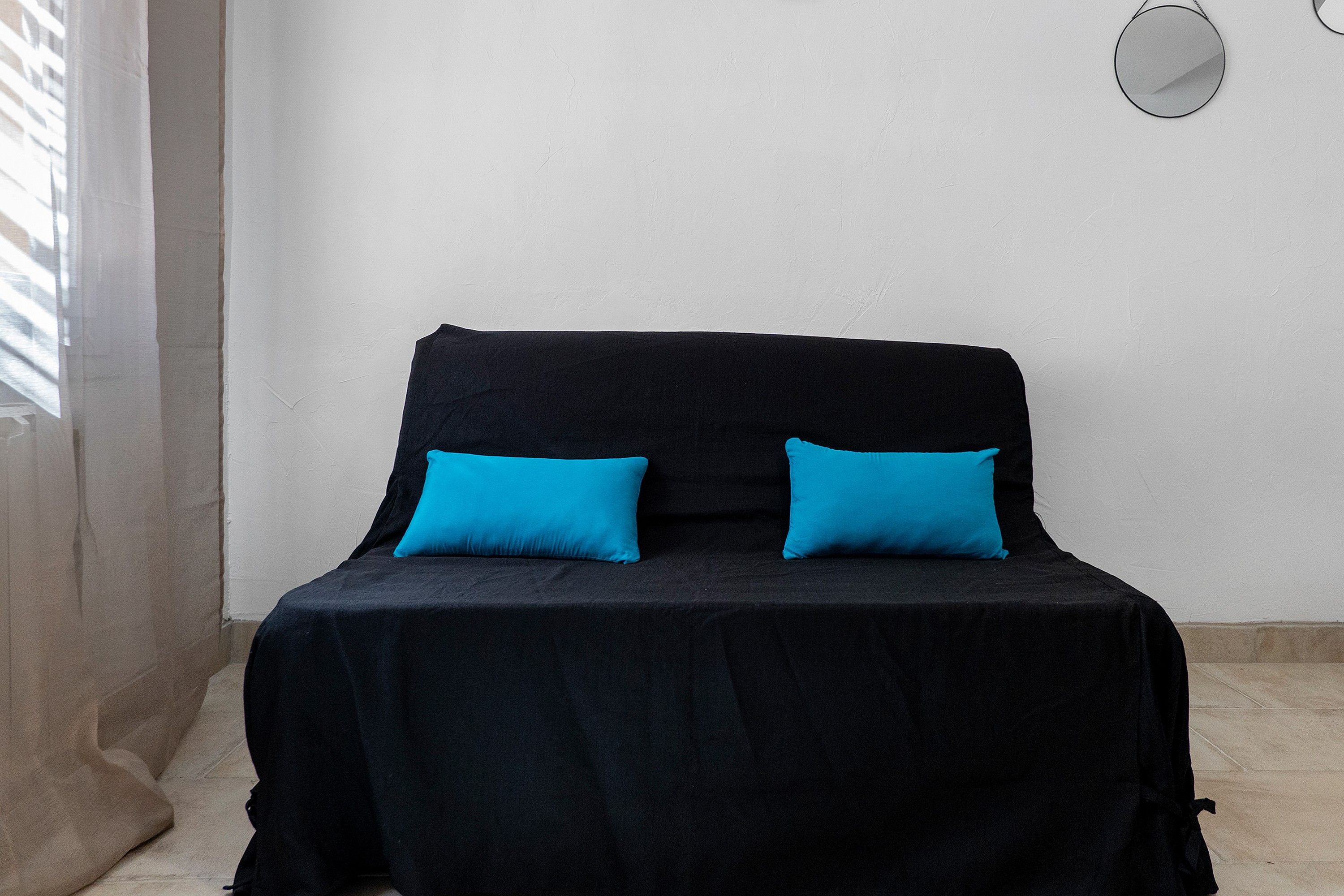 Een bed met een zwarte spreidek en twee felblauwe kussens.