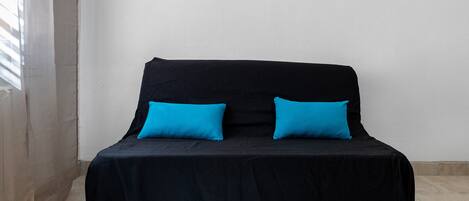 A bed with a black cover and two bright blue pillows.