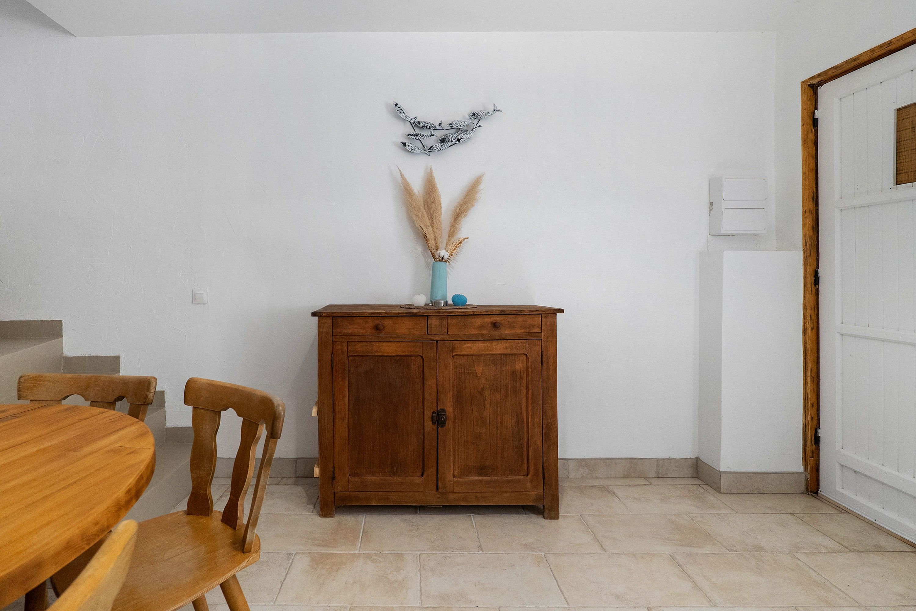 Ein Essbereich mit einem Holztisch und -stühlen, einem Schrank mit Dekoration und einer Tür rechts.