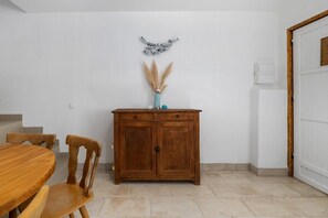 Un coin repas avec une table et des chaises en bois, un meuble contenant des objets décoratifs et une porte sur la droite.