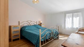 Ein Schlafzimmer mit einem Bett, Nachttischen, einer Lampe, einem Fenster mit Vorhängen und Holzboden.